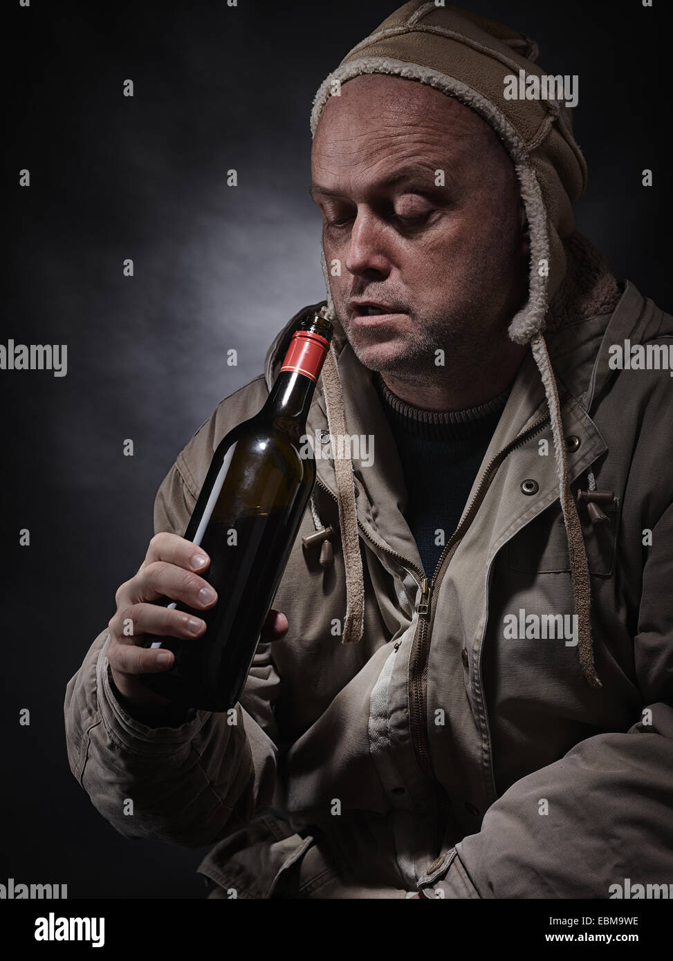 Middle aged alcoholic and wine bottle, he wearing winter clothings - vertical format Stock Photo