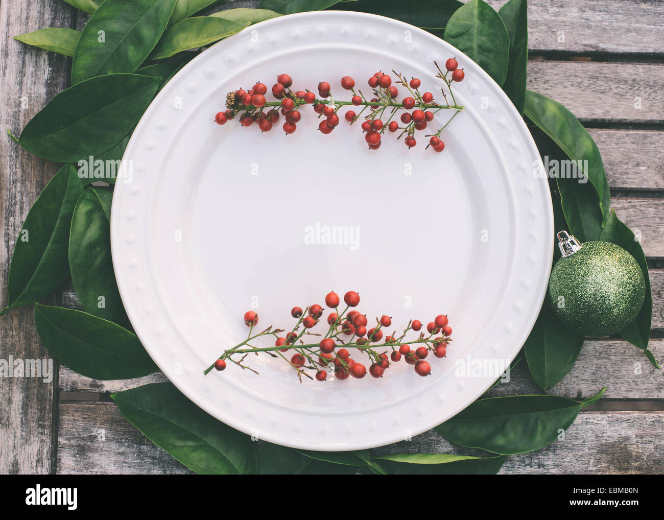 Rustic Christmas table setting with red berries bordering a white ... Rustic Christmas table setting with red berries bordering a white ...