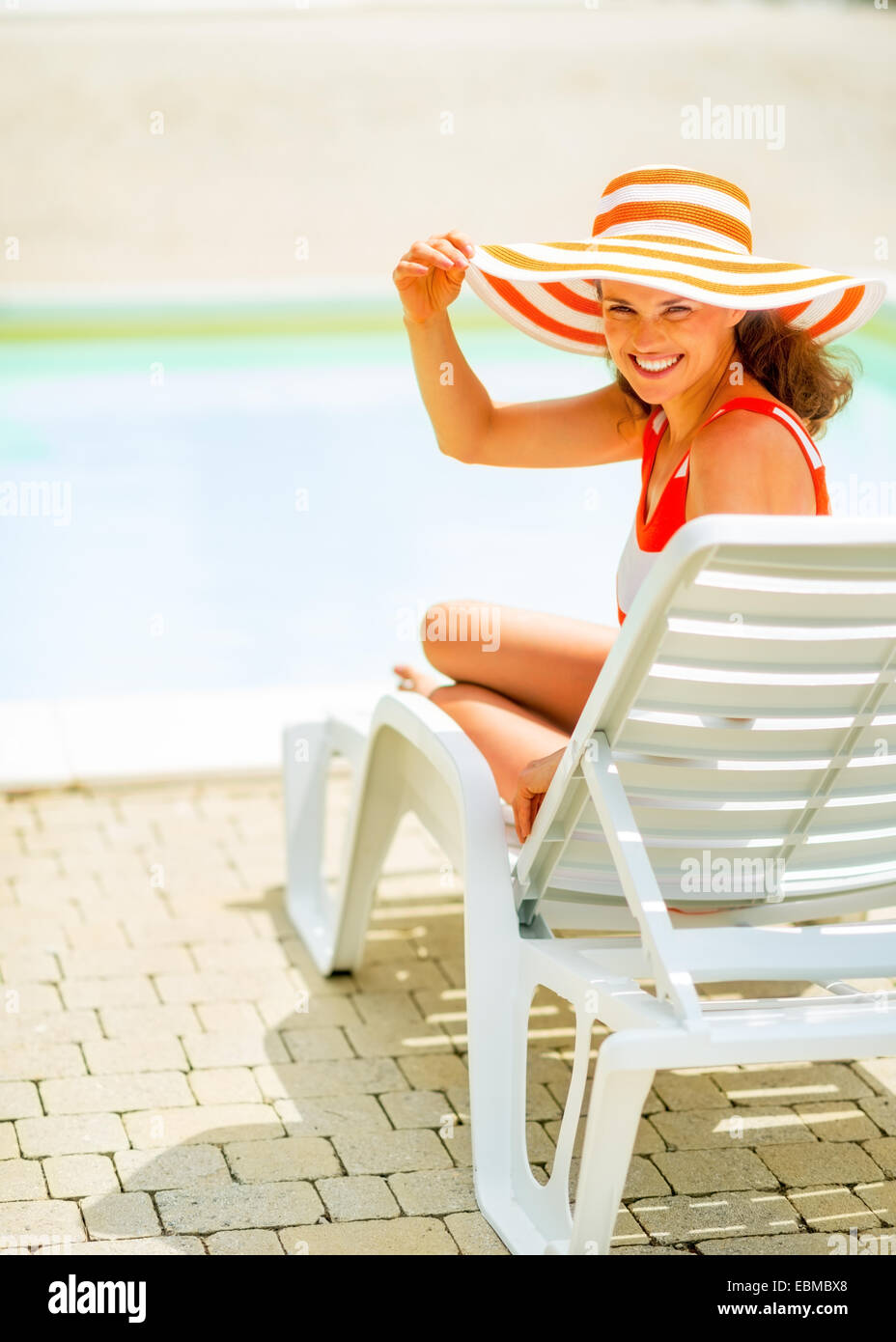 Smiling young woman in hat sitting on sunbed Stock Photo - Alamy