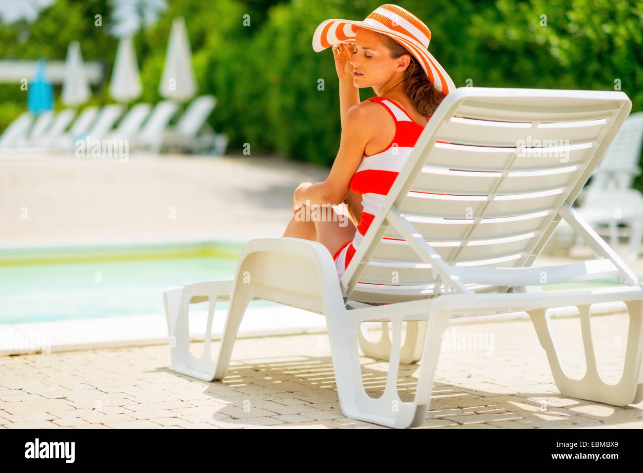 Relaxed young woman in hat sitting on sunbed. rear view Stock Photo - Alamy