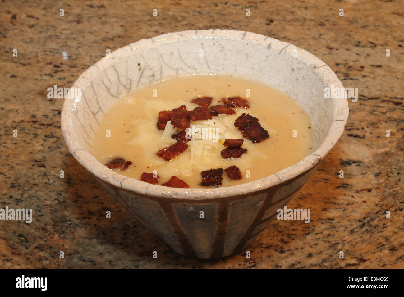 Horizontal image of homemade potato soup with bacon and white cheddar cheese in a striped, earthenware, cone-shaped bowl Stock Photo