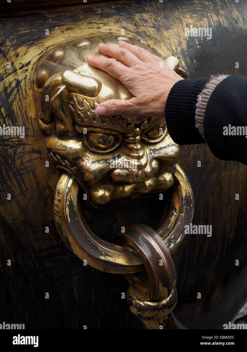 Hand rubbing a lion head on a giant cauldron inside the Forbidden City for good luck, Beijing, China Stock Photo