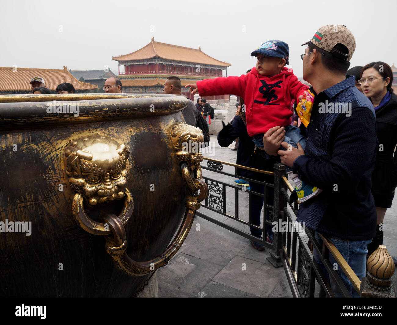 Young chinese boy rubbing the lion heads of a giant cauldron inside the Forbidden City for luck, Beijing, China Stock Photo