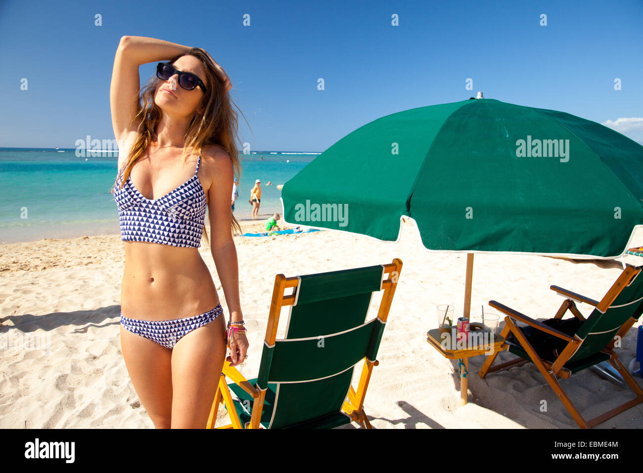 Attractive woman standing on beach in bikini near beach umbrella Stock Photo