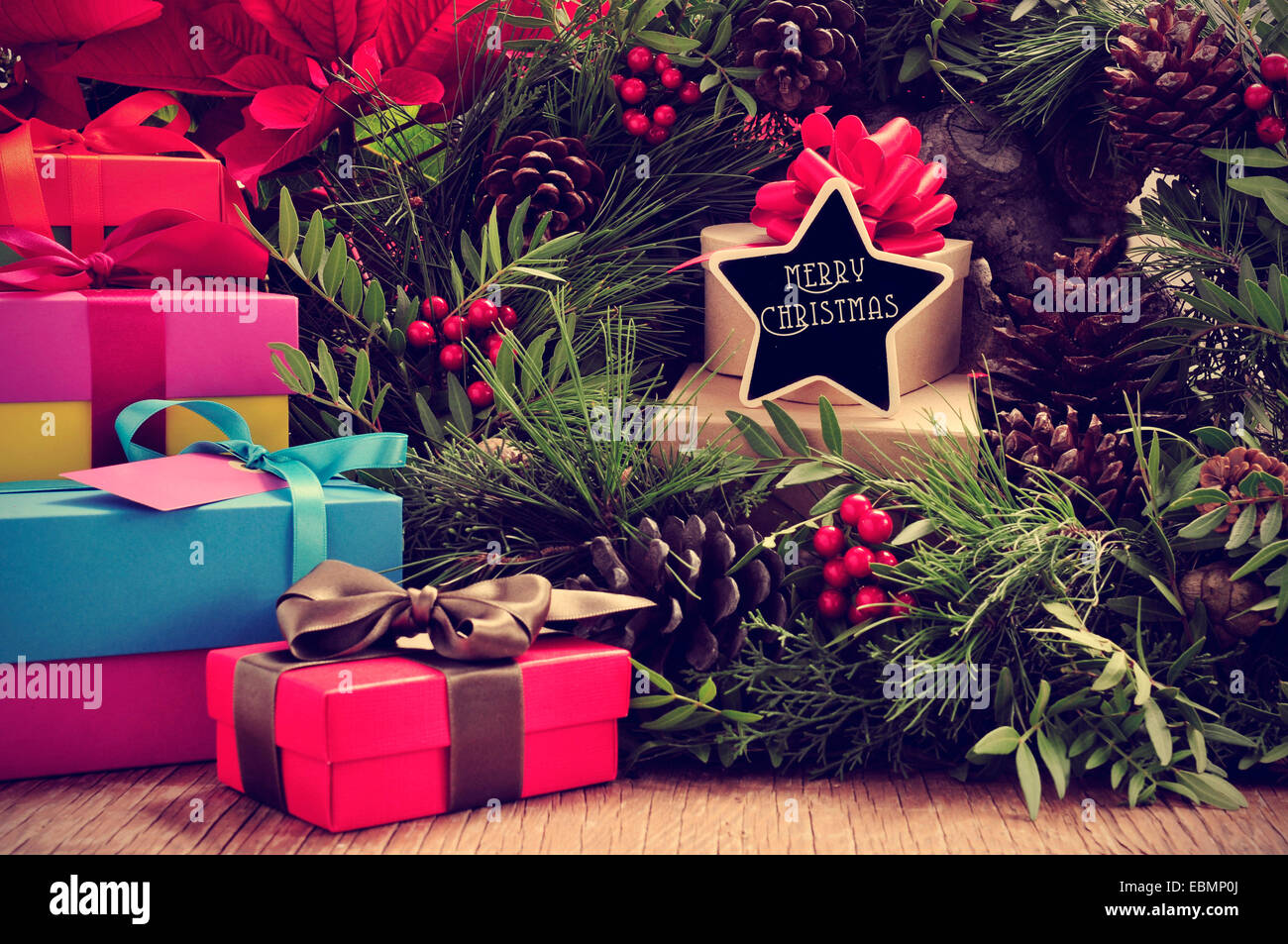 a pile of gifts and a natural christmas wreath with pine cones and red berries, and a star-shaped signboard with the text merry Stock Photo