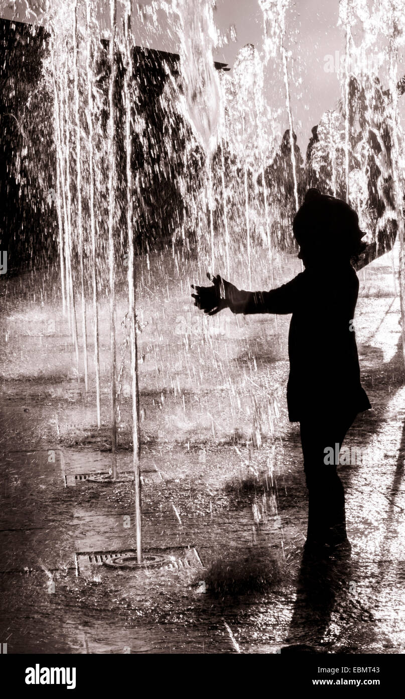 A silhouette of a little girl having playing with a water fountain ...