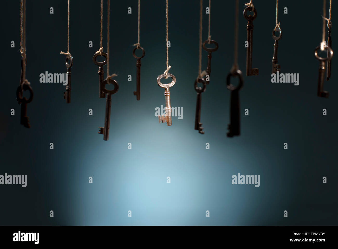 Old keys hanging on strings. One key in the middle is in spotlight focus. Stock Photo