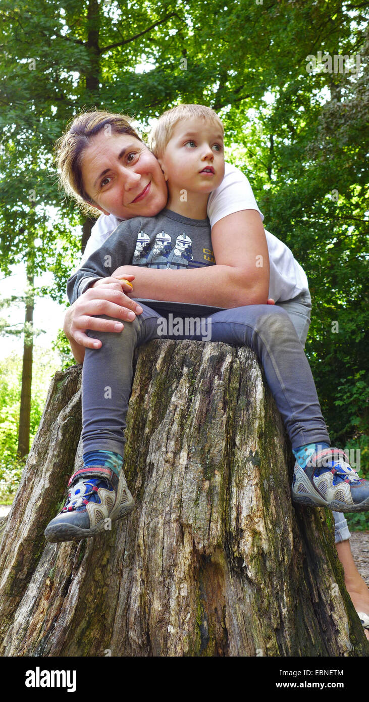 mother hugging her son sitting on a tree stump Stock Photo