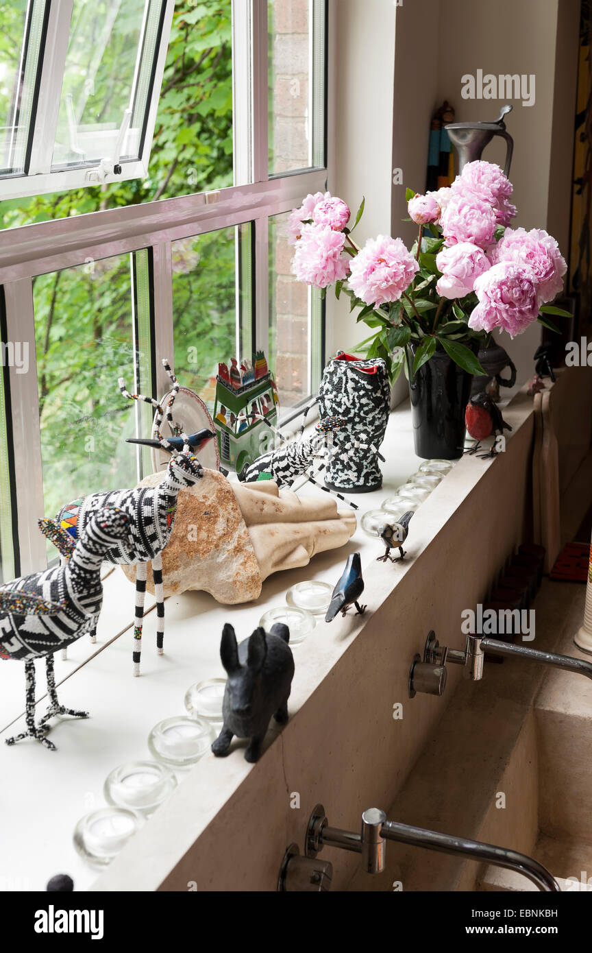 African bead animals and a vase of peonies on windowsill Stock Photo