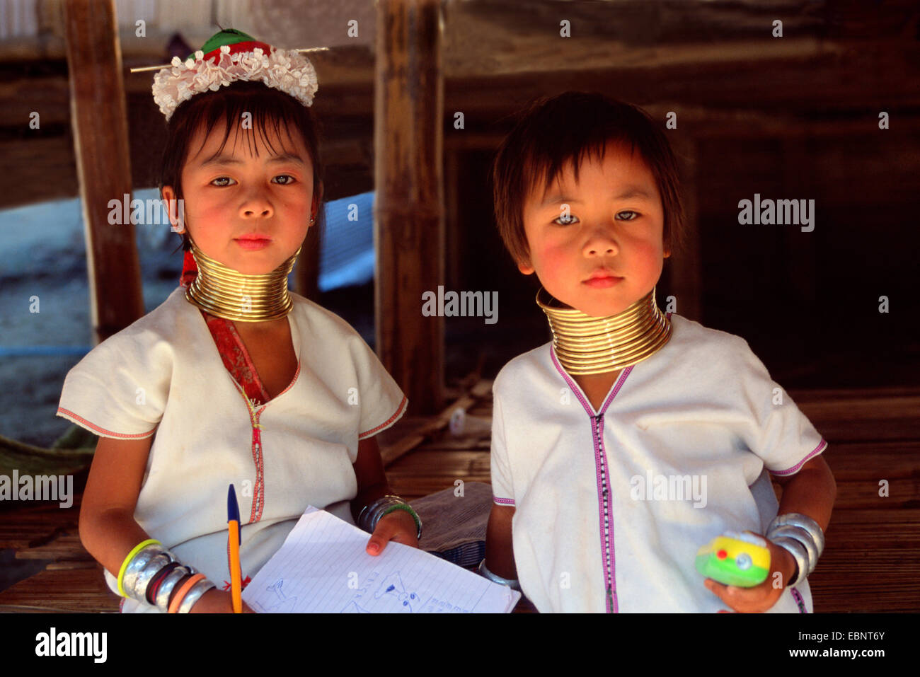 Hill tribe children in their national dress of golden rings and white shirts writing on a pad. Northern Thailand. Stock Photo