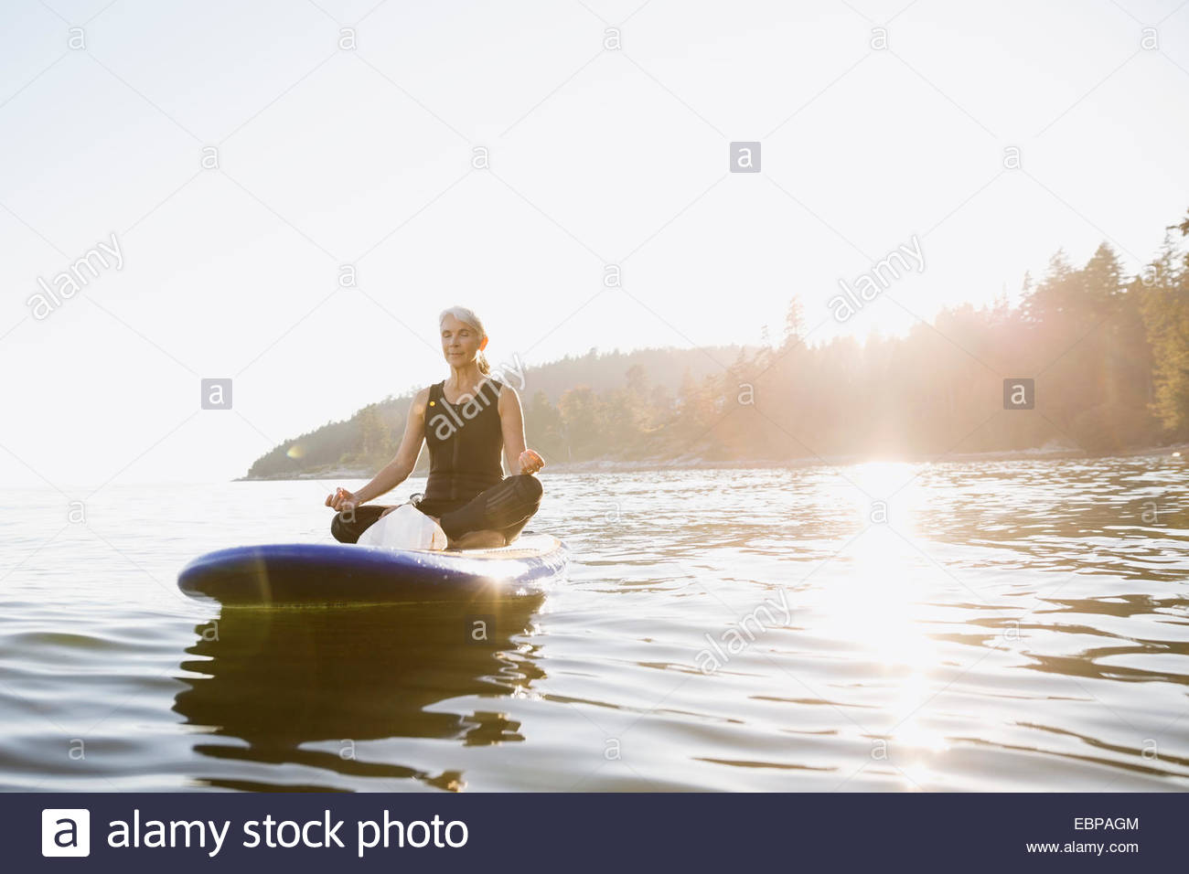 Senior woman meditating on paddle board in ocean Stock Photo