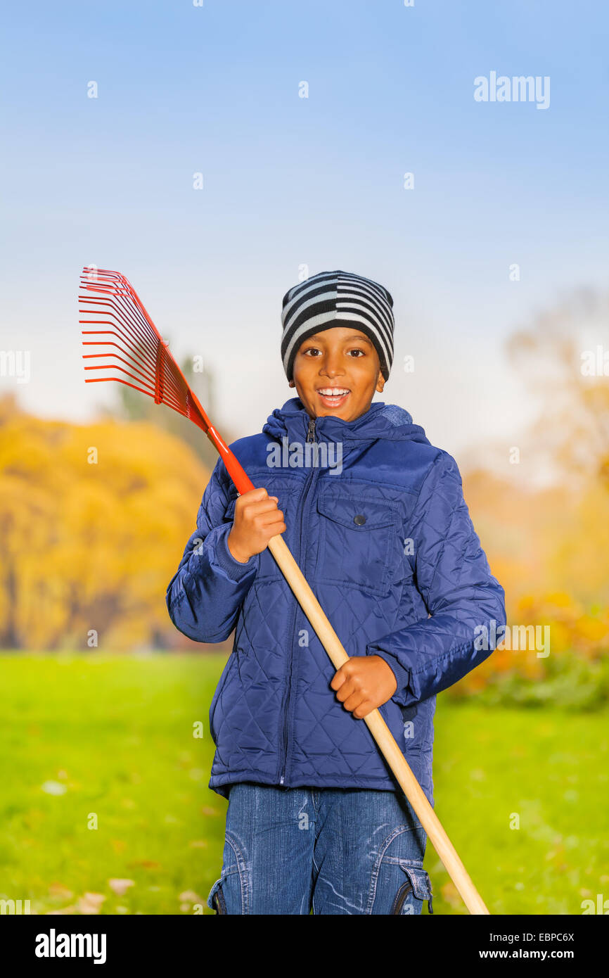 African smiling boy holds red rake in park Stock Photo Alamy