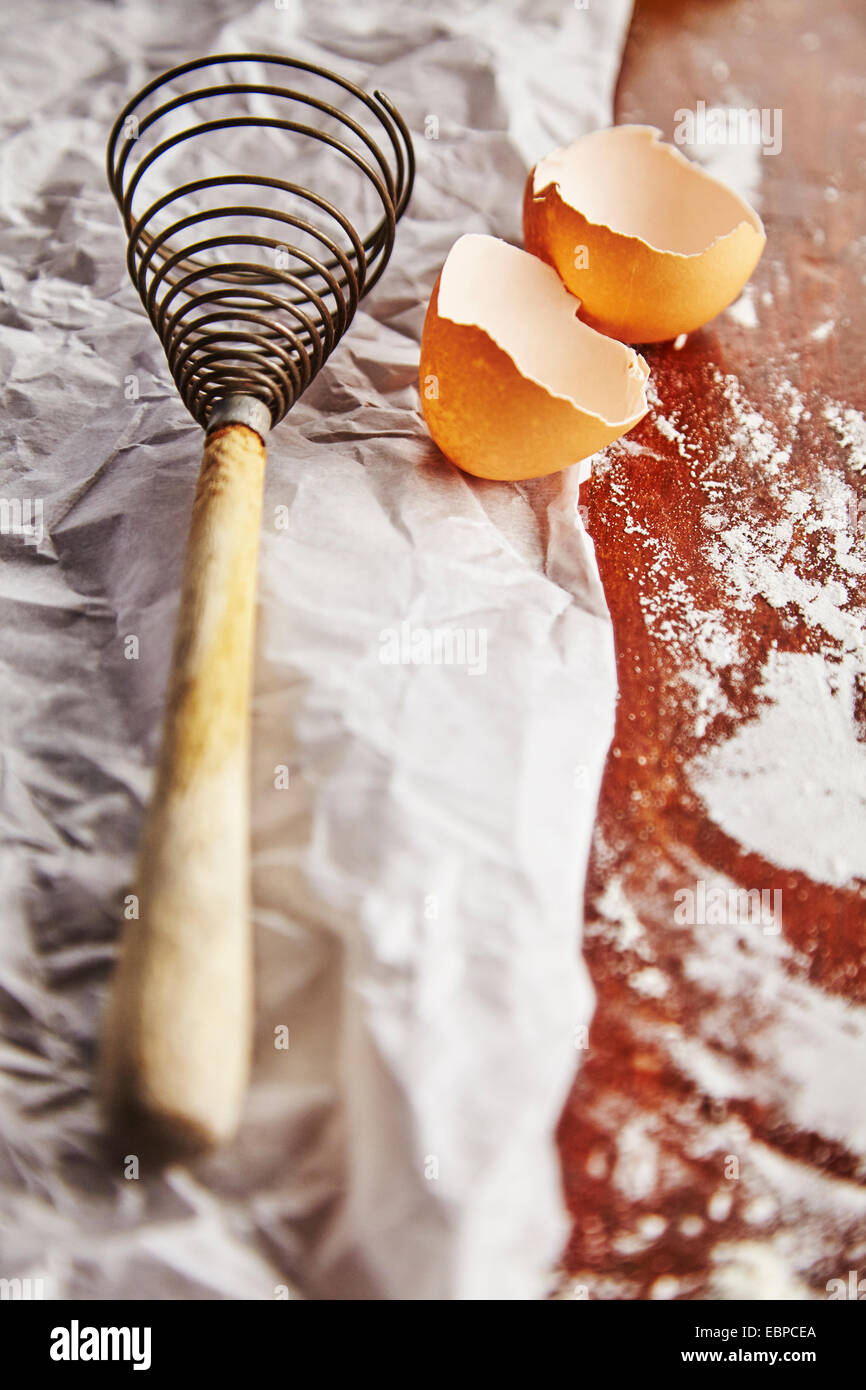 vintage whisk over a bowl with flour and an egg on top of parchment paper and wood table Stock Photo