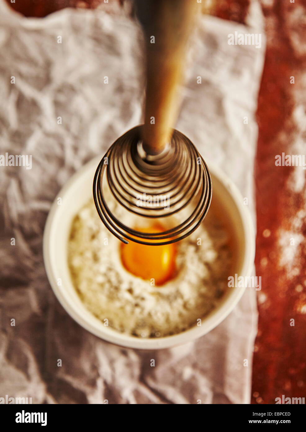 vintage whisk over a bowl with flour and an egg on top of parchment