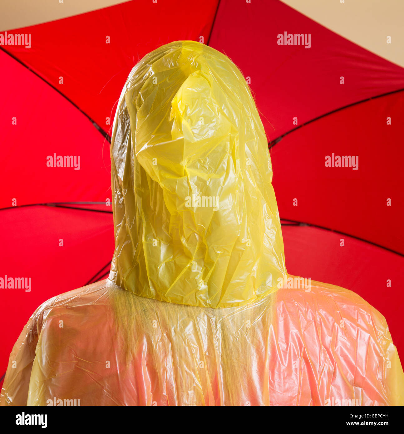 Woman wearing yellow poncho holding red umbrella Stock Photo
