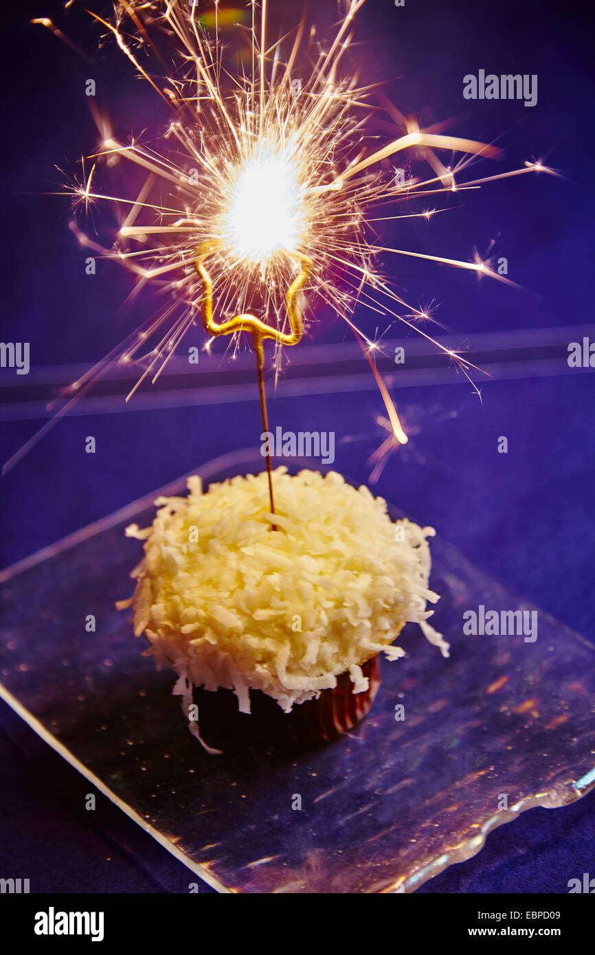 sparkler on a coconut cupcake on a glass plate dark background Stock Photo
