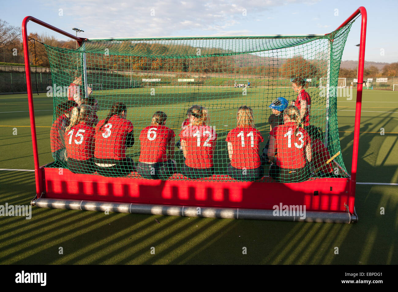 A ladies hockey team having a half-time talk from their coach while sitting in the goal. Stock Photo