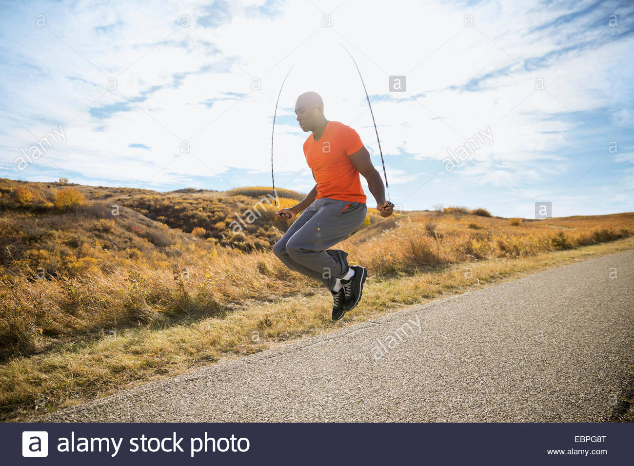Man jump roping on sunny rural path Stock Photo