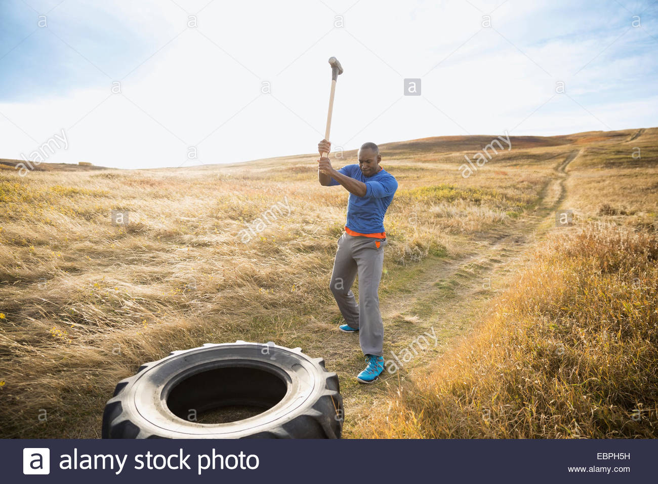 Man hammering crossfit tire in sunny rural field Stock Photo