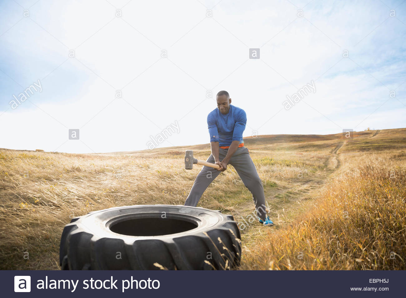 Man hammering crossfit tire in sunny rural field Stock Photo