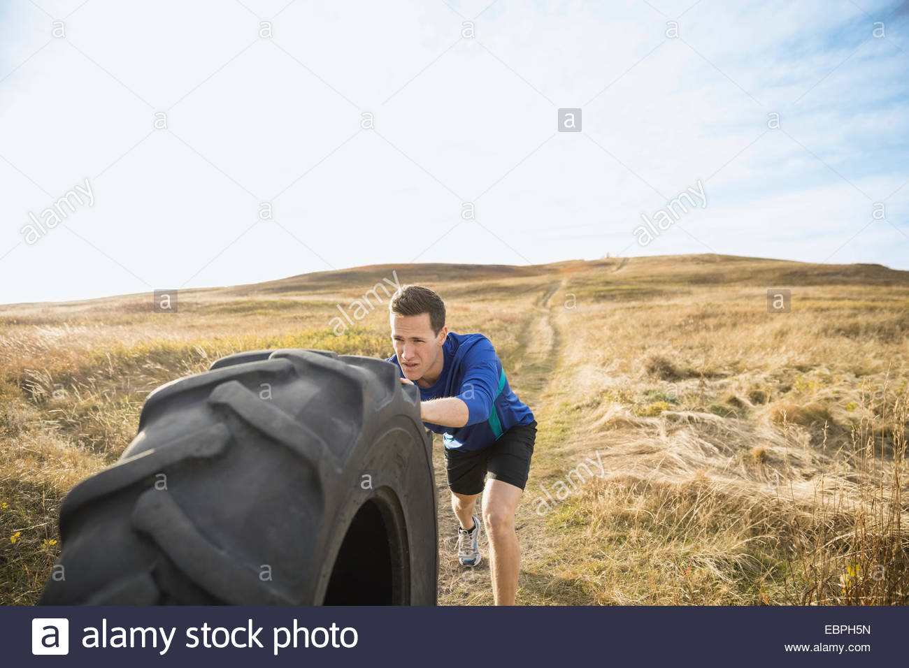 Man pushing crossfit tire in sunny rural field Stock Photo