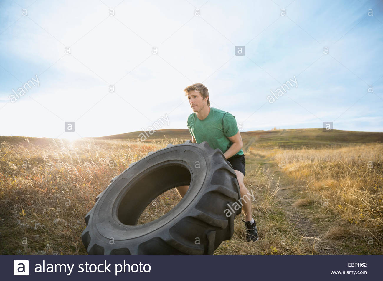 Man flipping crossfit tire in sunny rural field Stock Photo