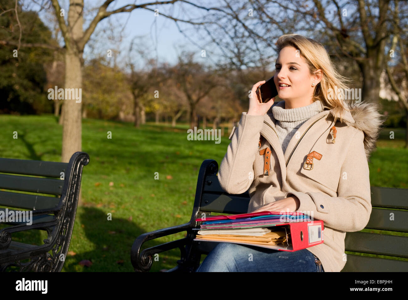 woman sitting on a park bench with folders and talking on the phone ...