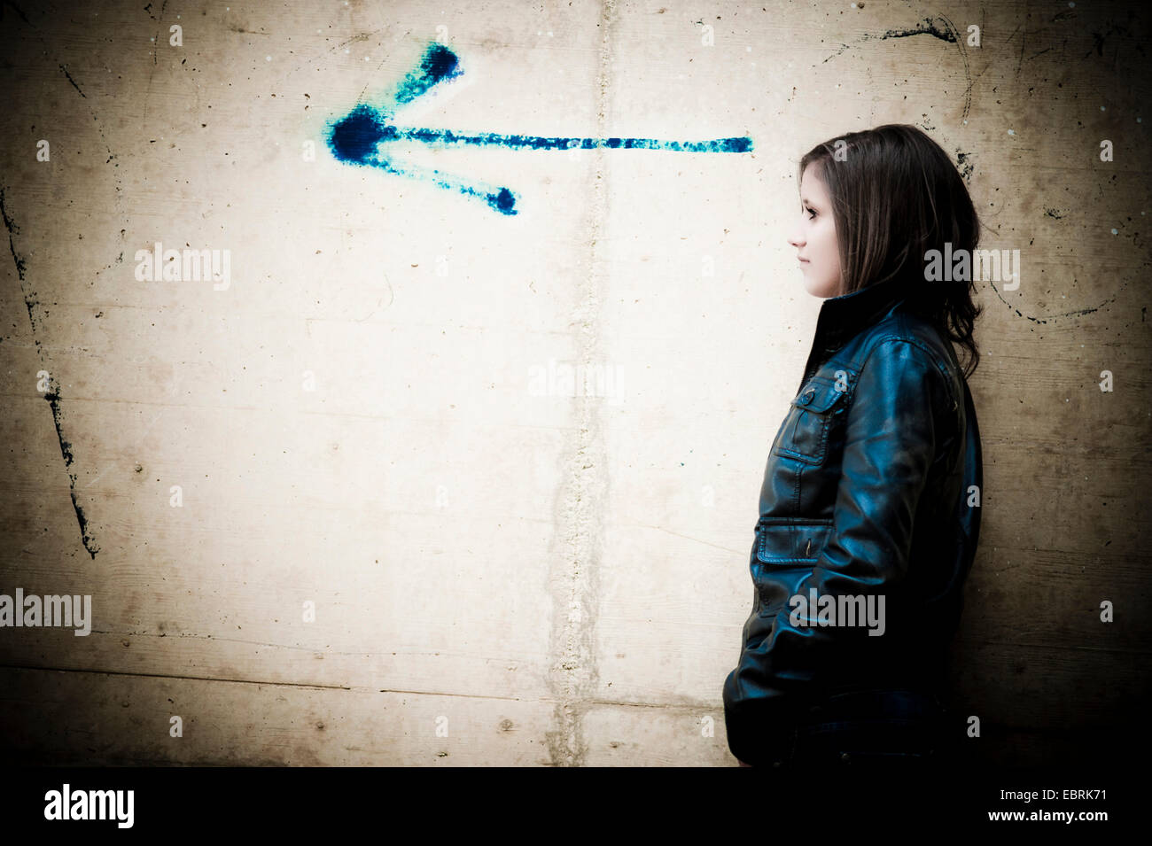 young girl standing looking into the direction of an arrow painted onto a concrete wall Stock Photo