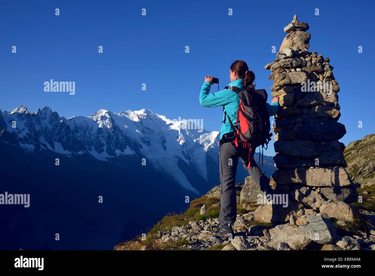 female mountain hiker taking a picture next ot a pile of stones in front of Mont Blanc, the highest summit of Europa, France, Haute-Savoie Stock Photo