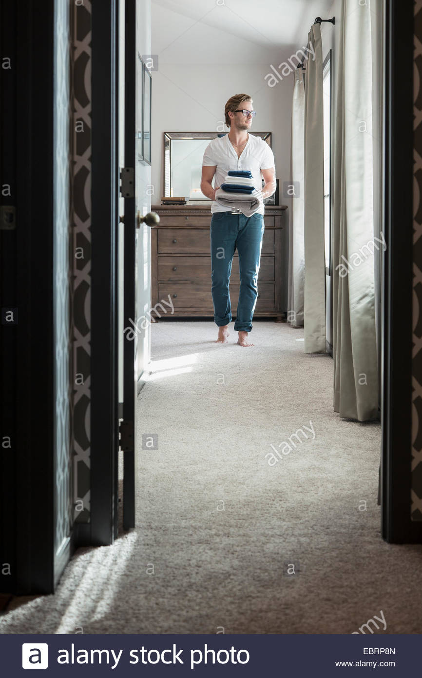 Man carrying towels in bedroom Stock Photo