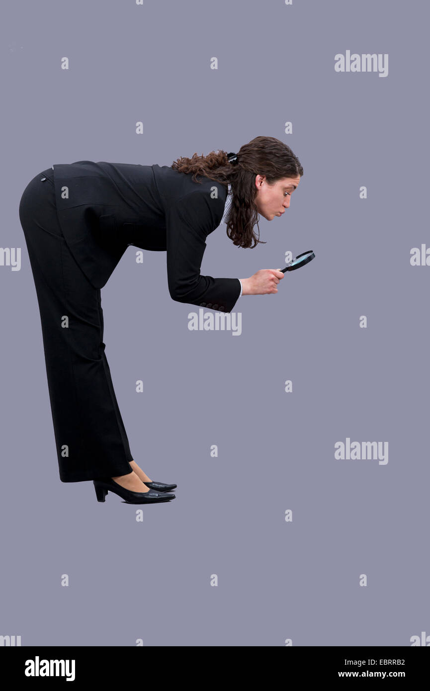 young woman in a black pantsuit standing bent down examining the ground with a loupe Stock Photo
