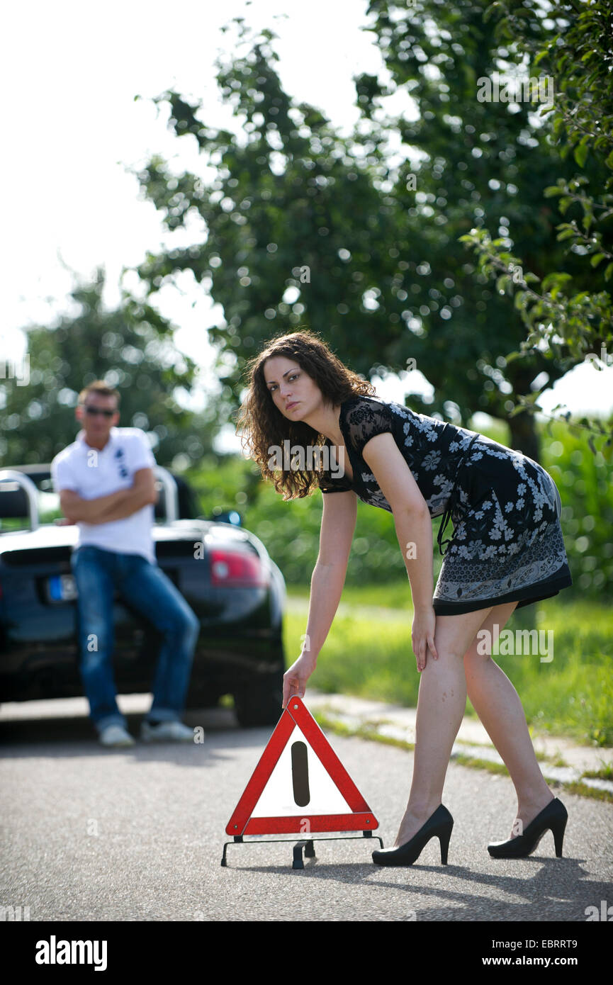 young woman putting up a warning triangle with a smile after a breakdown on a country road, Germany Stock Photo
