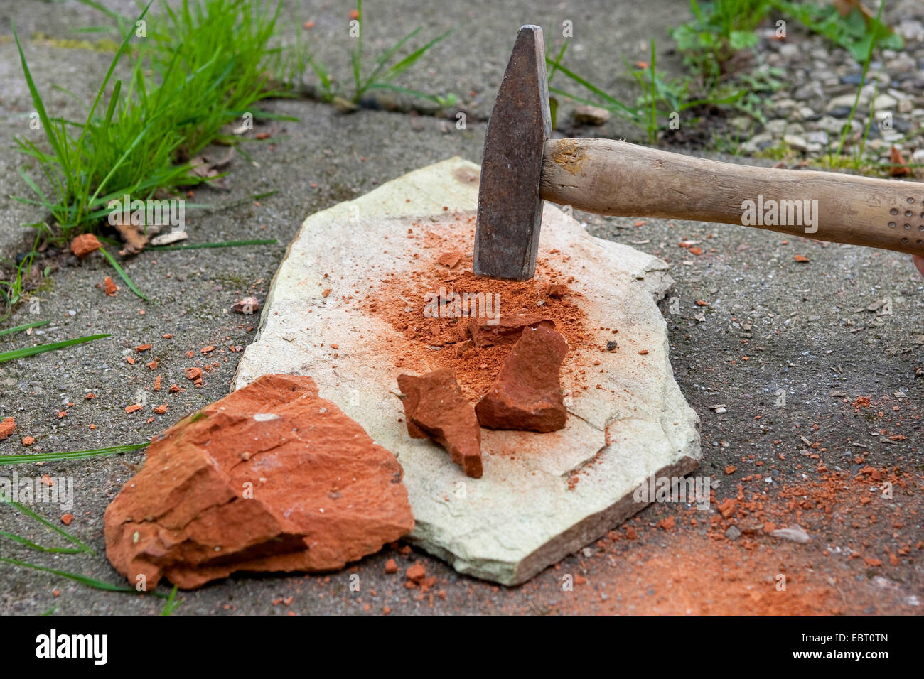 crushing a red sandstone with a hammer to paint with earth colour, Germany Stock Photo