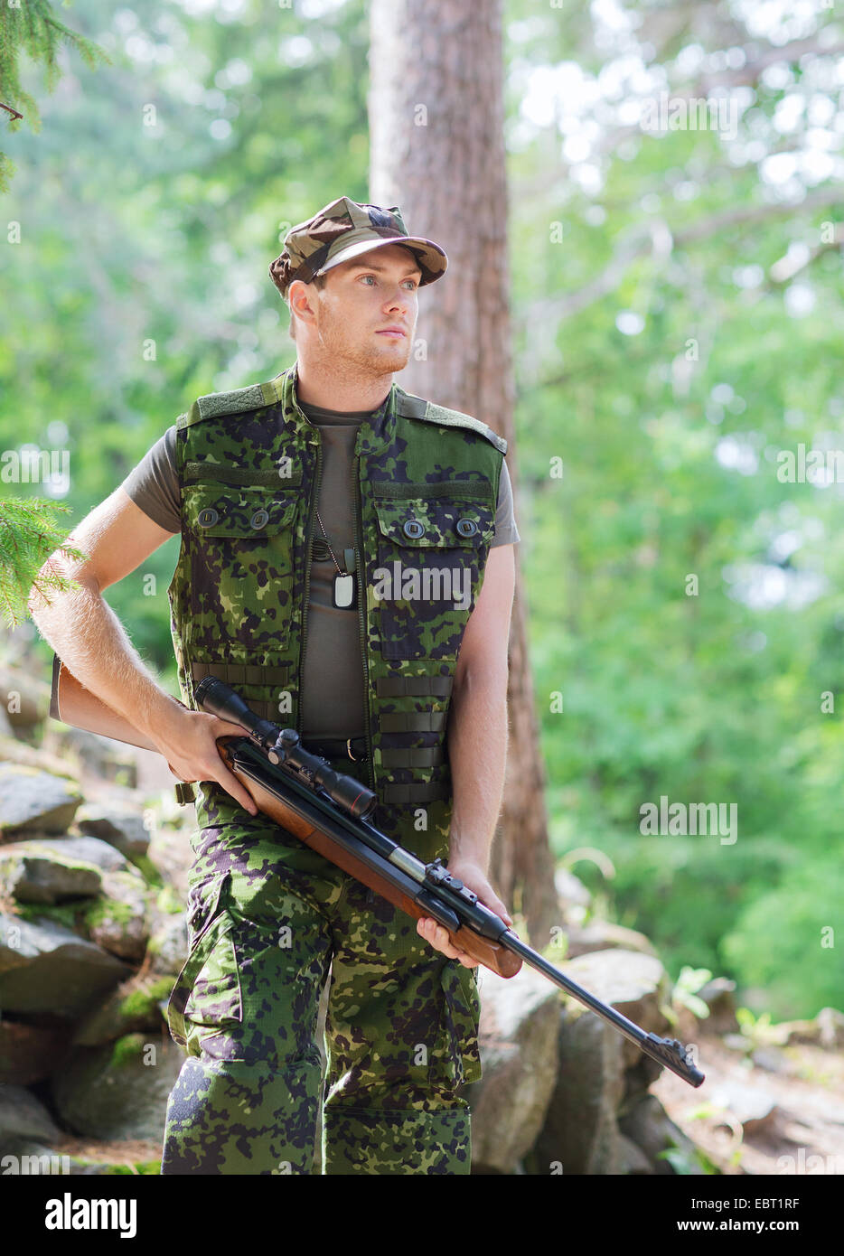young soldier or hunter with gun in forest Stock Photo