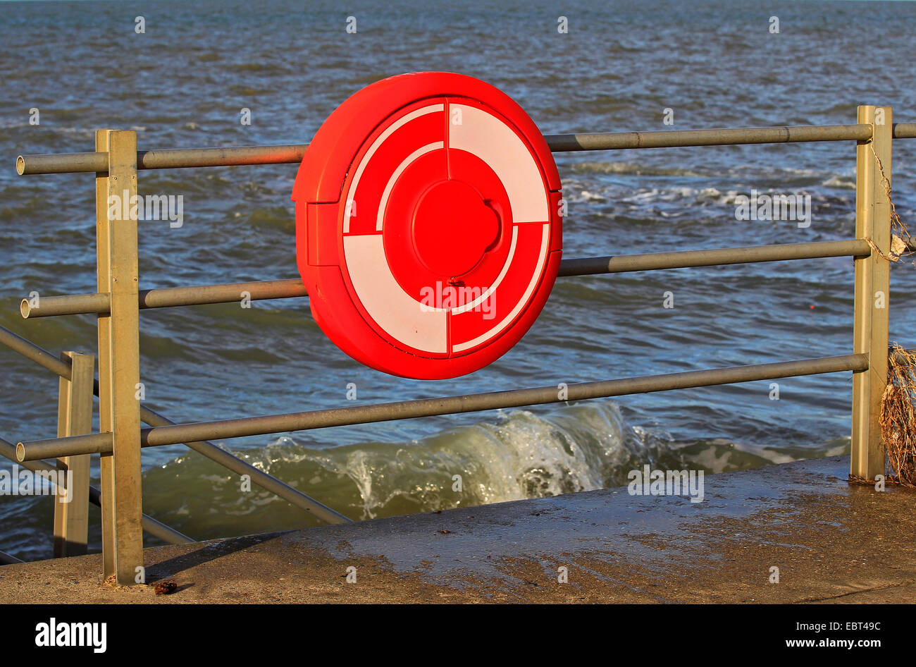 East Kent coast - Minnis Bay, England - Bright red lifebuoy attached to a metal fence on the promenade with sea at high tide Stock Photo