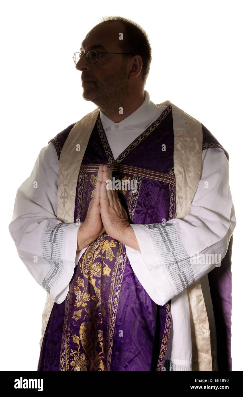 symbol picture for 'abuse in the (catholic) church': half length portrait of a praying priest in a cassock with the head in the shadow Stock Photo
