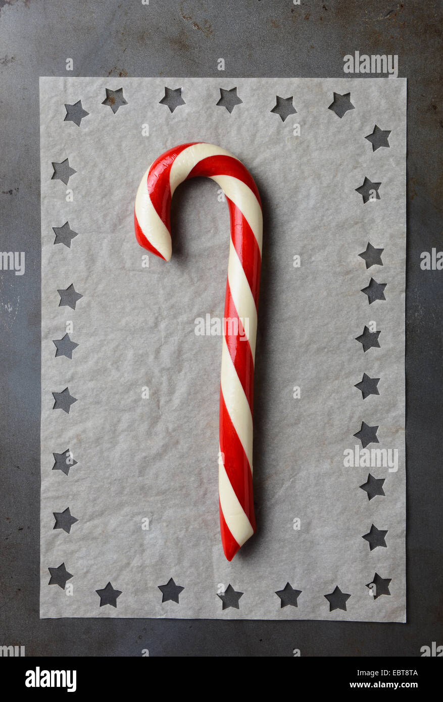 Closeup high angle shot of an old fashioned candy cane on parchment paper with star shapes cut into the papers edge. Vertical fo Stock Photo