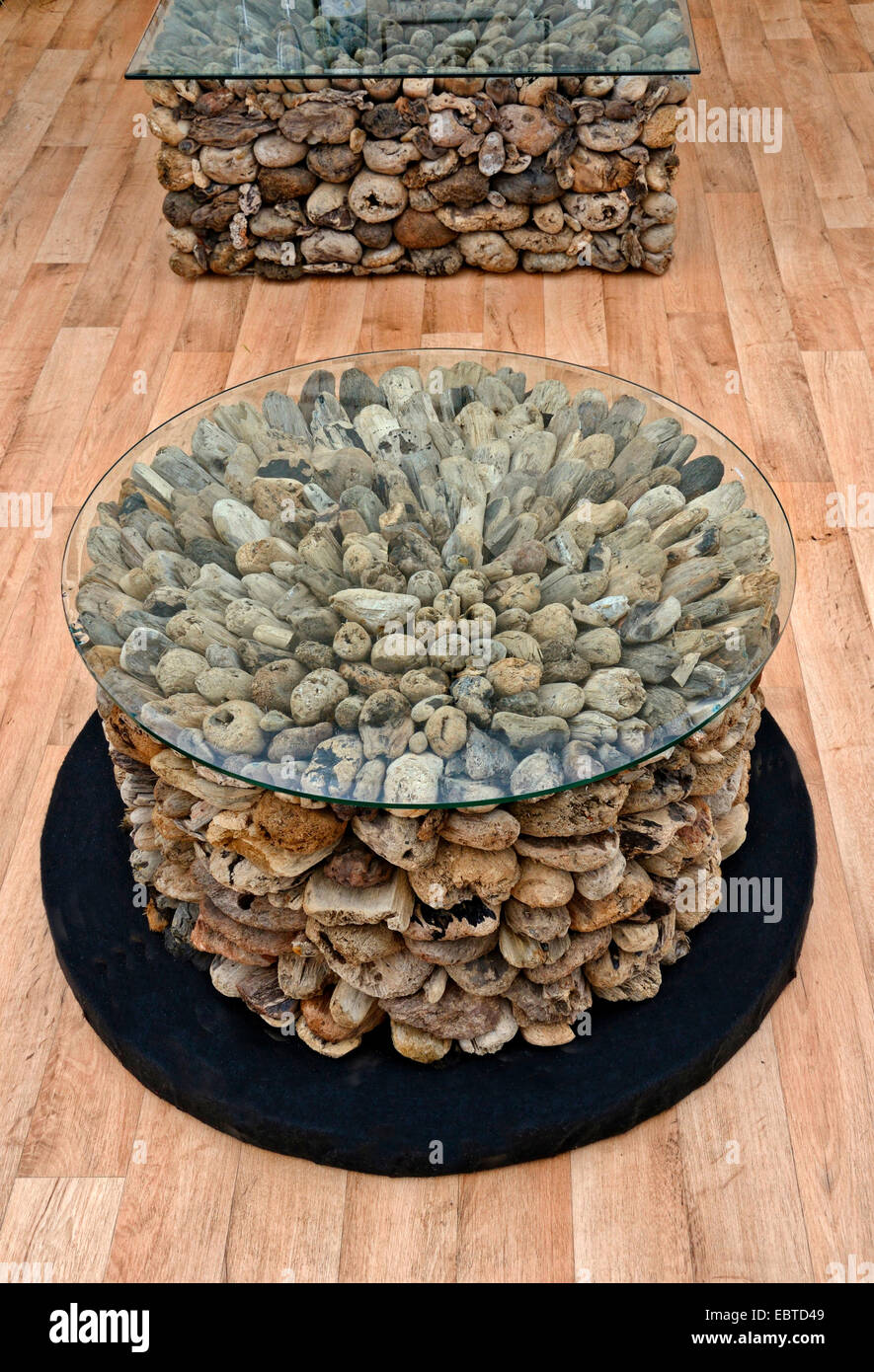 Modern glass topped coffee tables with a decorative base made of driftwood on a decking floor Stock Photo