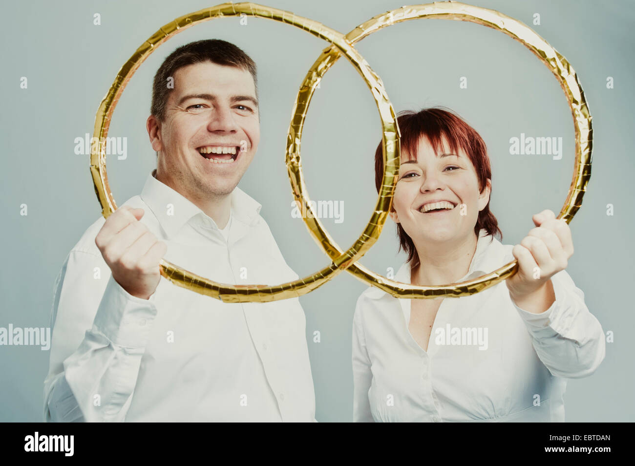 young couple happily looking through oversize wedding rings Stock Photo