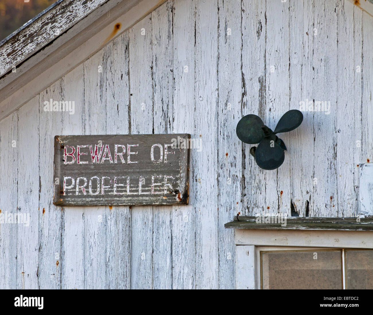 funny arrangement at the wall of a wooden house with a small old ship's propeller and an old wooden sign saying 'beware of propeller', Norway, Vest-Agder, Lista, Farsund Stock Photo
