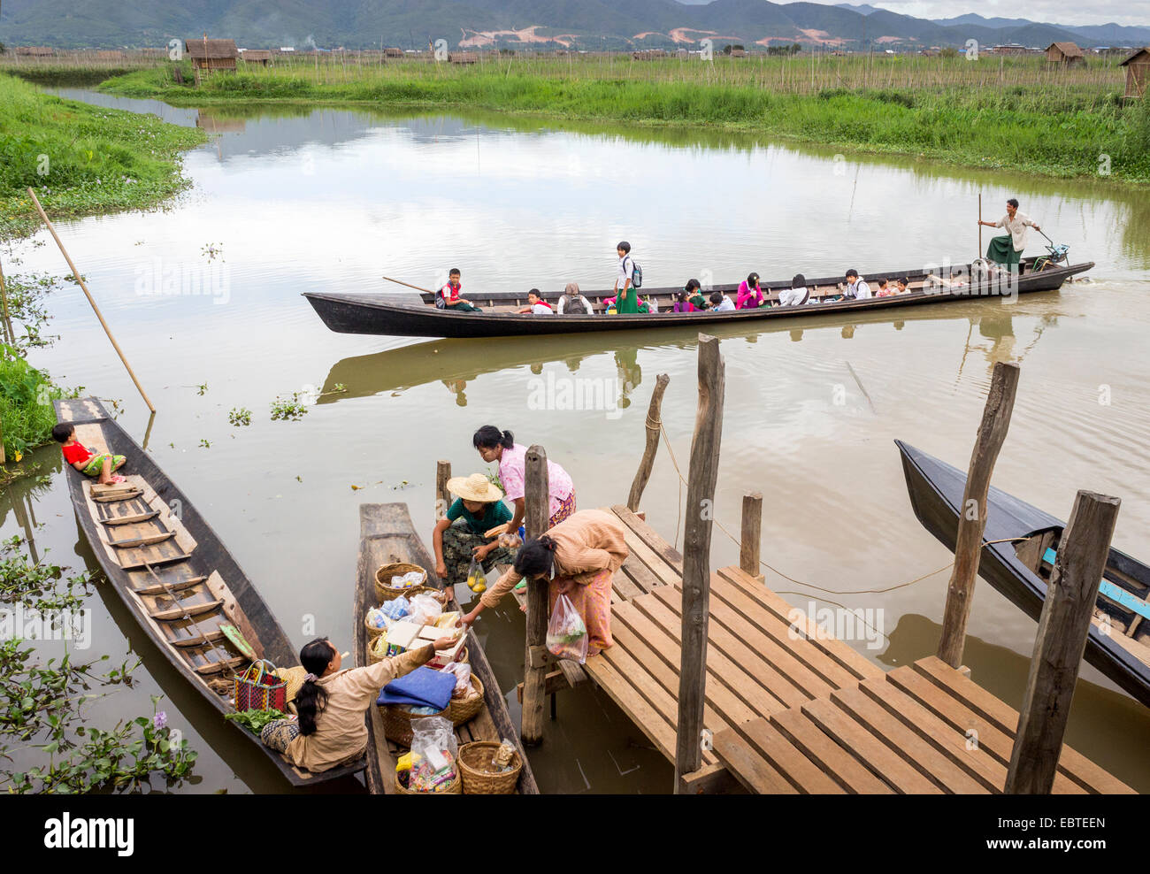 women selling and buying from a floating shop on lake Inle in Burma, Myanmar and children in uniform traveling back from school Stock Photo
