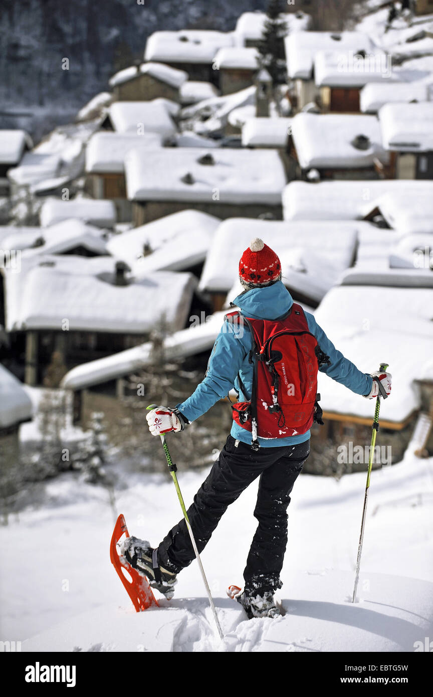 woman with snow shoes standing in front of snowy mountain village, France, Savoie, Le Miroir Stock Photo