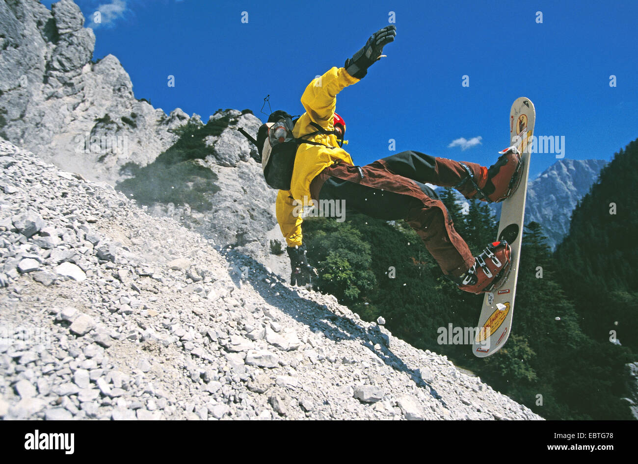 man falling while 'rockboarding' in the mountains (going down a gravel slope on a snowboard) Stock Photo