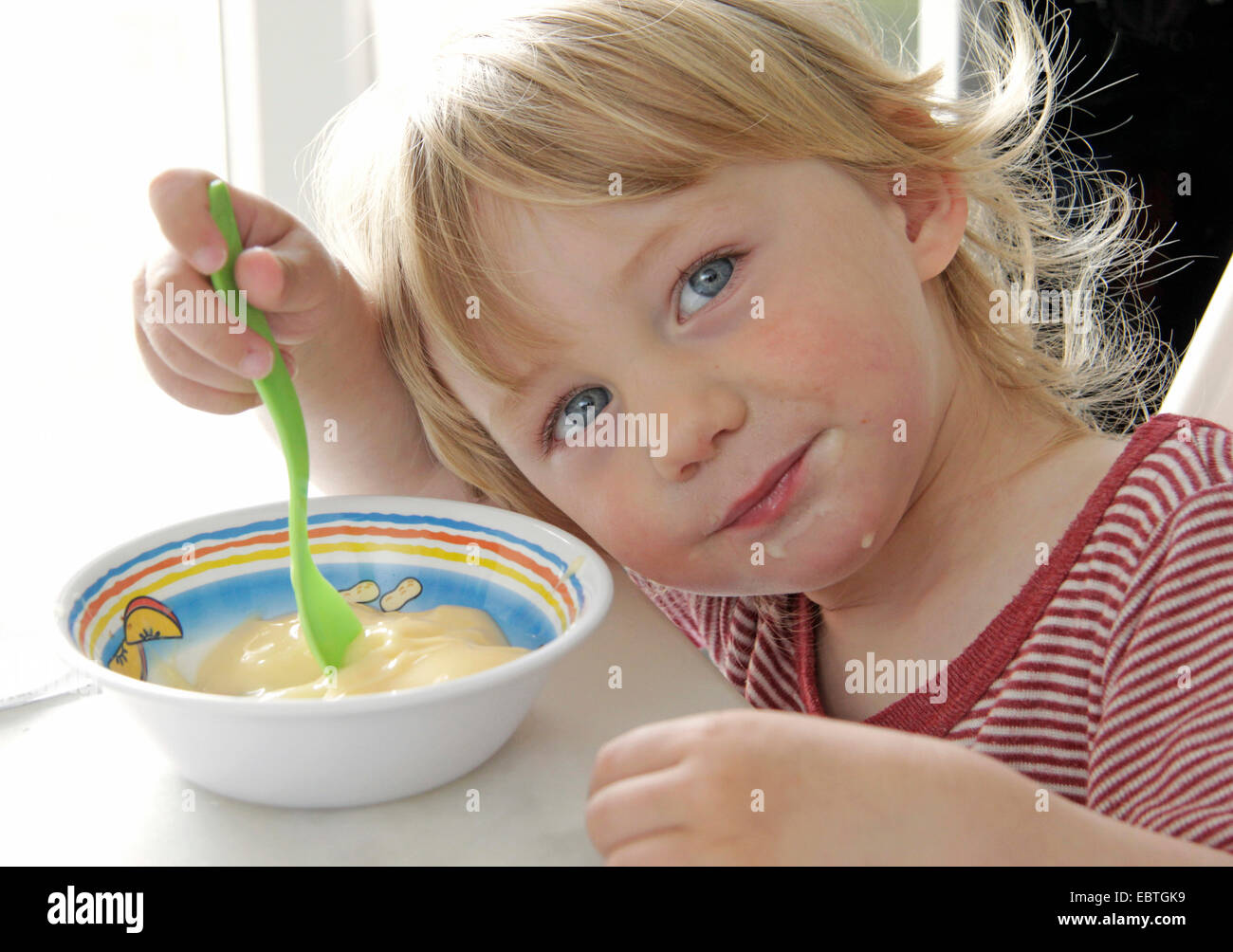 little boy sitting at the table and eating custard, Germany Stock Photo