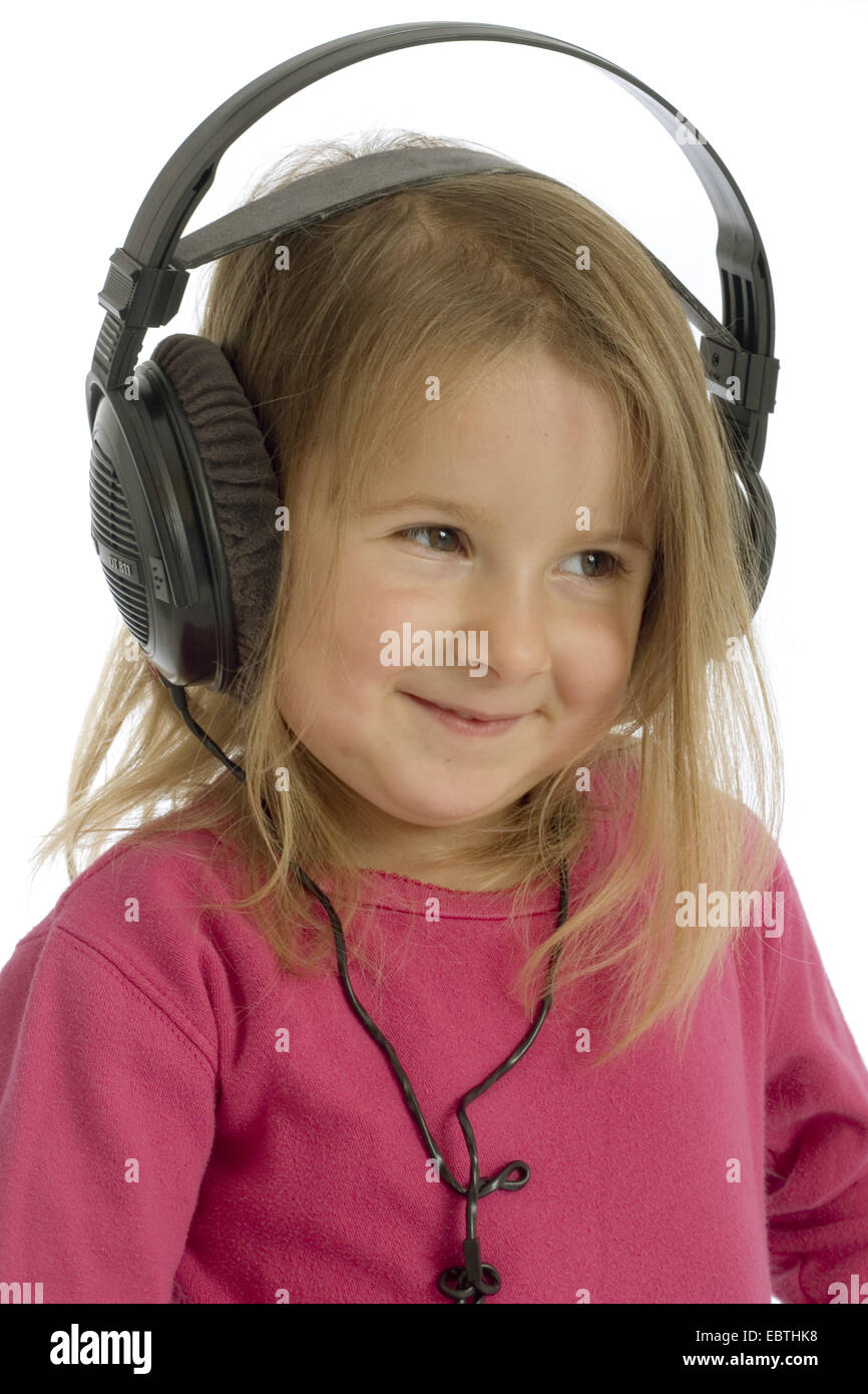 little girl smiling while listening to something by earphones Stock Photo