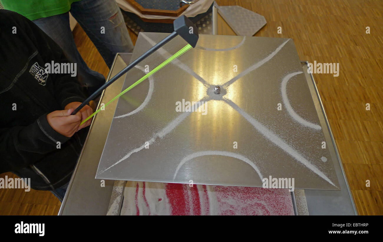 physical demonstration with sand forming a pattern when someone is sweeping along a metal sheet where it's lying on with a bow Stock Photo