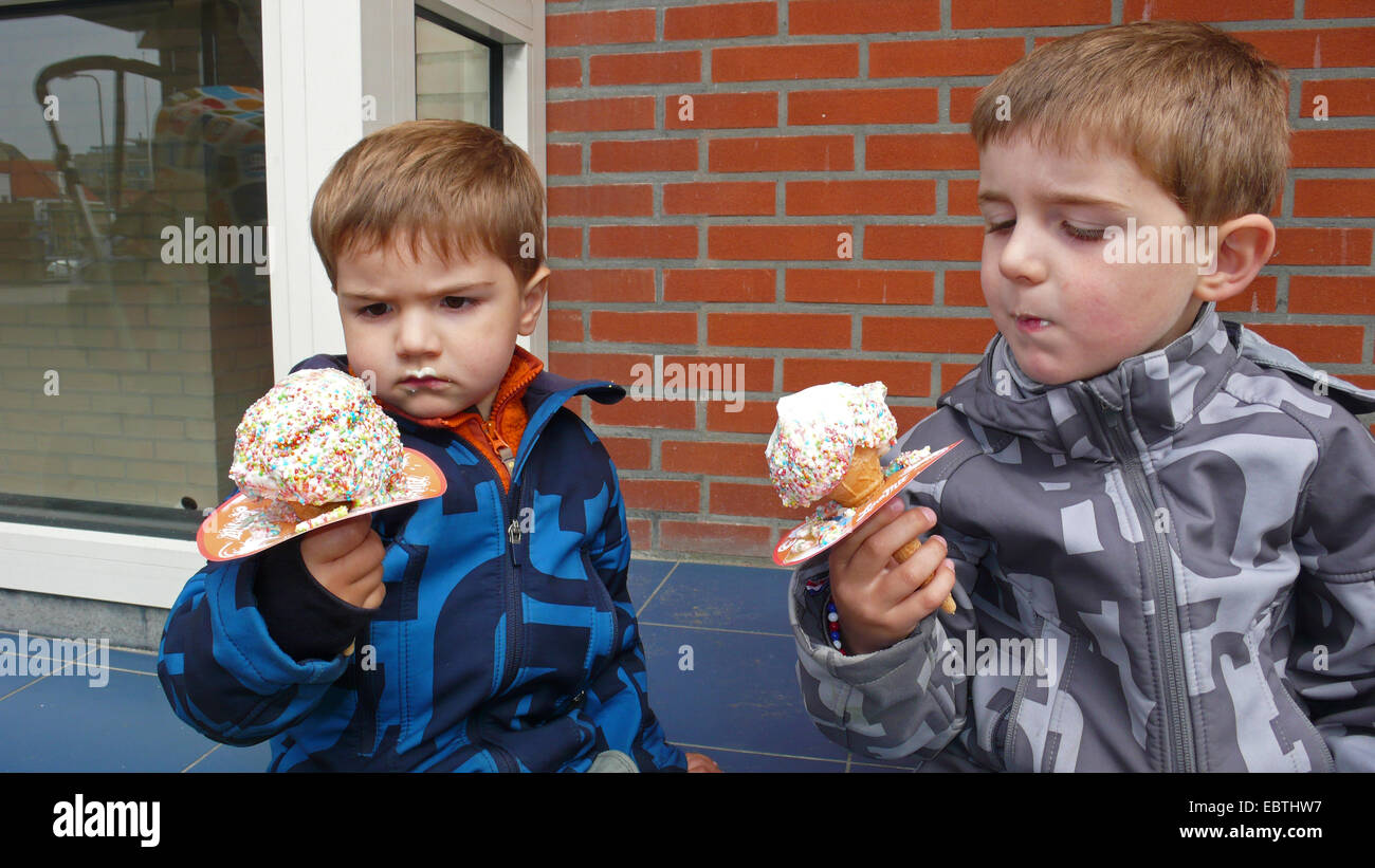 little boys suspiciously eating a cone ice-cream with a paper sleeve to avoid dribbling Stock Photo