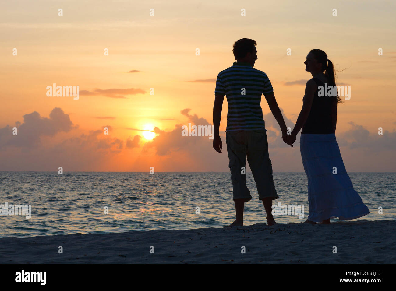 Silhouette of a couple holding hands on beach at sunset hi-res stock ...