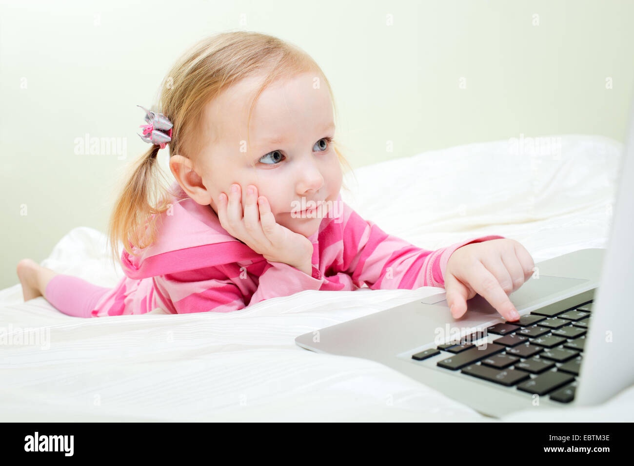 little girl lying in bed in front of a laptop Stock Photo