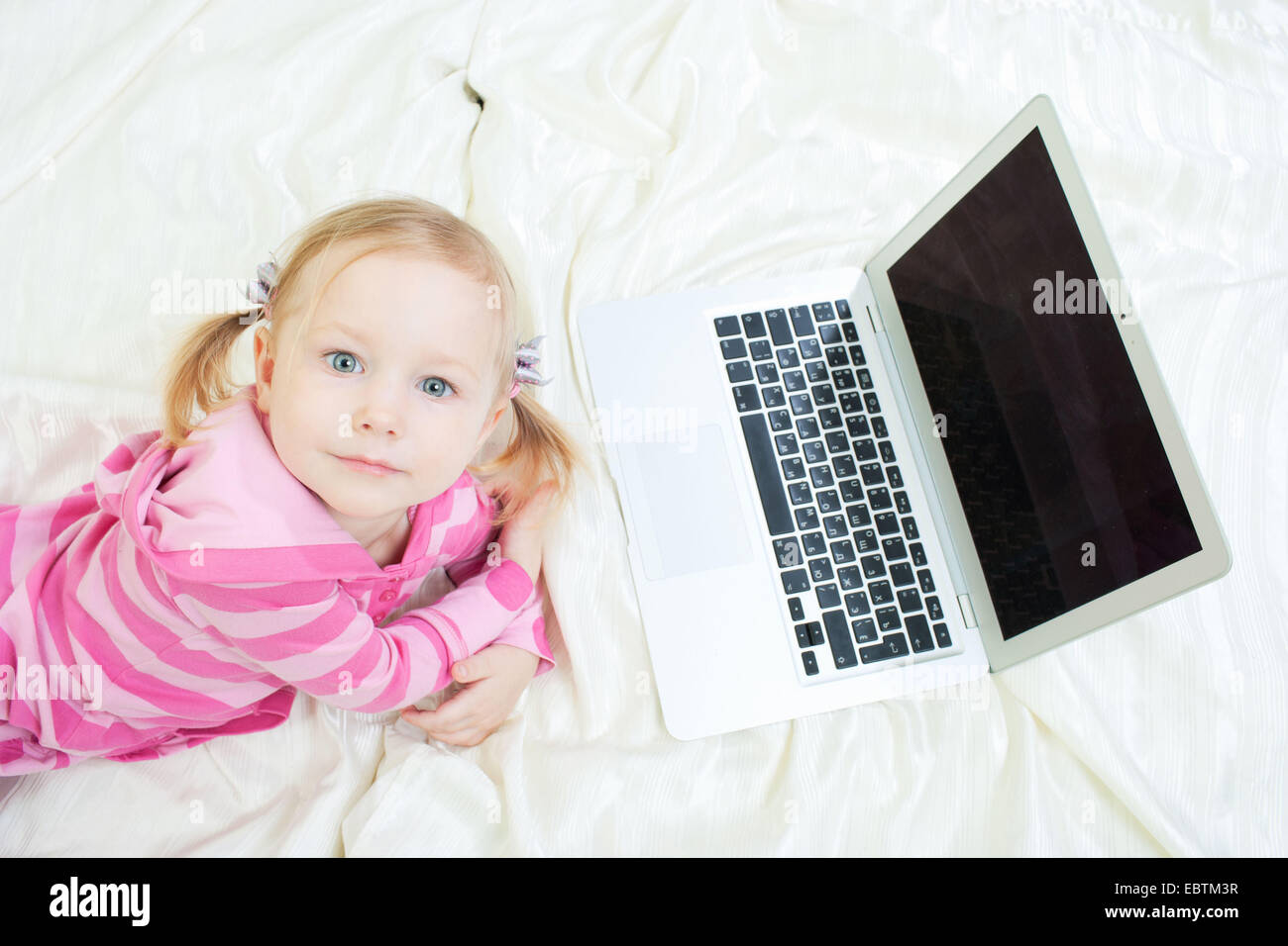 little girl lying in bed in front of a laptop Stock Photo